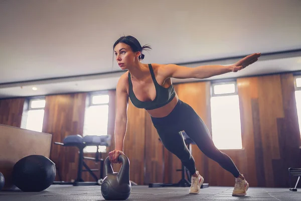 Joven chica motivada haciendo ejercicio tablón usando kettlebells con — Foto de Stock