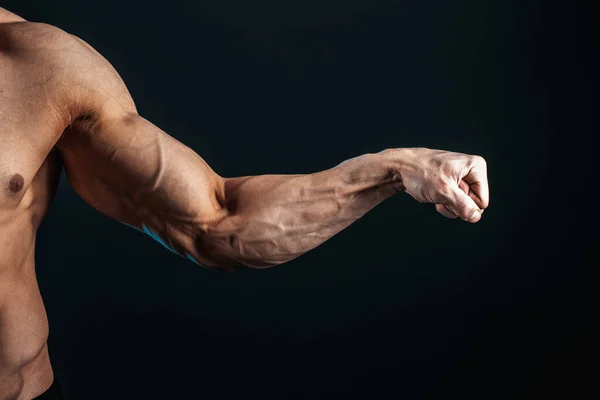Braccio teso stretto in pugno, vene, muscoli bodybuilder su uno sfondo scuro, isolare — Foto Stock