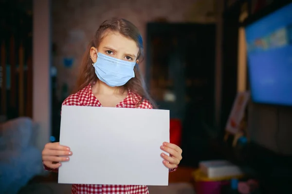 Liten flicka i en skyddande mask, pyjamas håller ett tomt ark av — Stockfoto