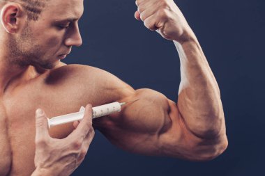 Vücut geliştirici vitamin enjeksiyonu yapar. Siyah arka planda mükemmel fiziği olan sporcu bir adamın fotoğrafı. Kuvvet ve motivasyon