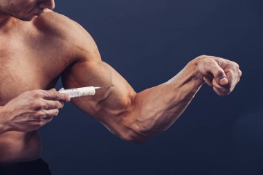 Vücut geliştirici vitamin enjeksiyonu yapar. Siyah arka planda mükemmel fiziği olan sporcu bir adamın fotoğrafı. Kuvvet ve motivasyon