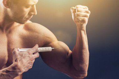 Vücut geliştirici vitamin enjeksiyonu yapar. Siyah arka planda mükemmel fiziği olan sporcu bir adamın fotoğrafı. Kuvvet ve motivasyon