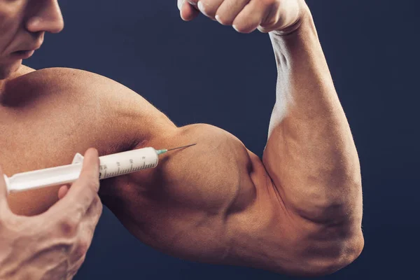 Bodybuilder makes injection of vitamins. Photo of sporty man with perfect physique on dark background. Strength and motivation — Stock Photo, Image