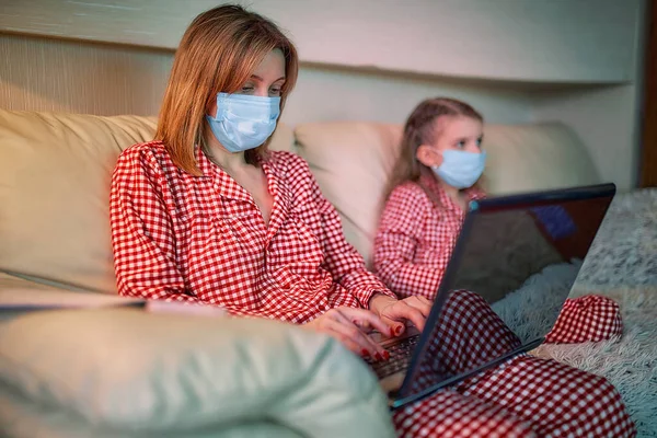 Kvinna i pyjamas med anteckningsbok och papper som arbetar hemifrån bär skyddsmask medan hennes barn, dotter spelar datorkonsol spel — Stockfoto