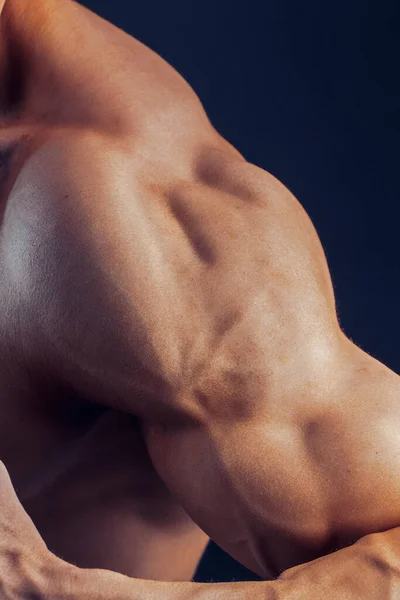 Fitness man achtergrond schouder biceps borstspieren triceps bodybuilder op een donkere achtergrond demonstreert de fysieke vorm voor lessen in de sportschool — Stockfoto