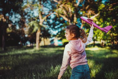 Küçük kız parkın dışındaki havaya oyuncak bir uçak fırlatıyor. Çocuk oyuncak bir uçak fırlatıyor. Güzel küçük kız çimlerin üzerinde durur ve pembe oyuncak bir uçak fırlatır..