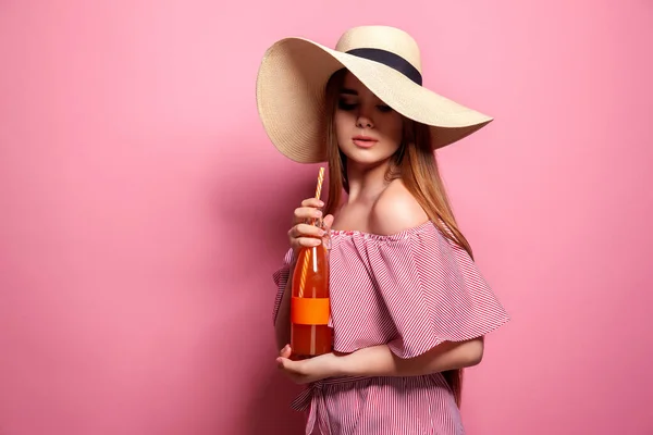 Foto von charmanten Frau trägt Strohhut trinken Saft aus Glasflasche isoliert über rosa Hintergrund. — Stockfoto