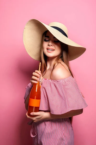 Foto de mujer encantadora con sombrero de paja bebiendo jugo de botella de vidrio aislado sobre fondo rosa. — Foto de Stock