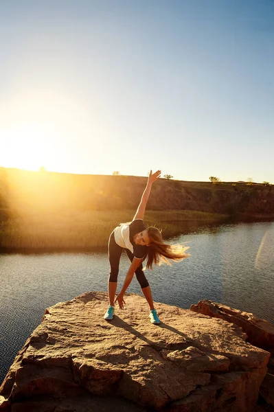 Joven mujer delgada practicando yoga al aire libre en la orilla de piedra del río de montaña. Unidad con el concepto de naturaleza —  Fotos de Stock