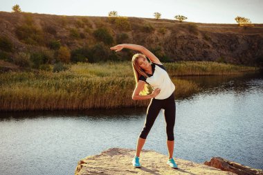 Genç, sıska kadın dağ nehrinin taştan kıyısında yoga yapıyor. Doğa kavramıyla birlik