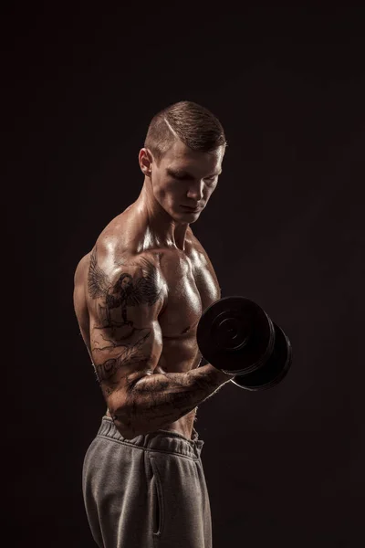 Serios tatuados atleta sin camisa levantamiento mancuernas entrenamiento sobre fondo oscuro — Foto de Stock