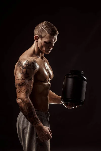 Sportovní zázemí. Silný kulturista drží plastovou nádobu se suchým proteinem Izolované. Sportovní jídlo — Stock fotografie