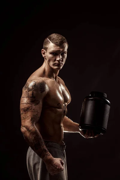 Spor geçmişleri. Güçlü bir vücut geliştirici, izole edilmiş proteinle plastik bir kavanoz tutuyor. Spor yemeği. — Stok fotoğraf