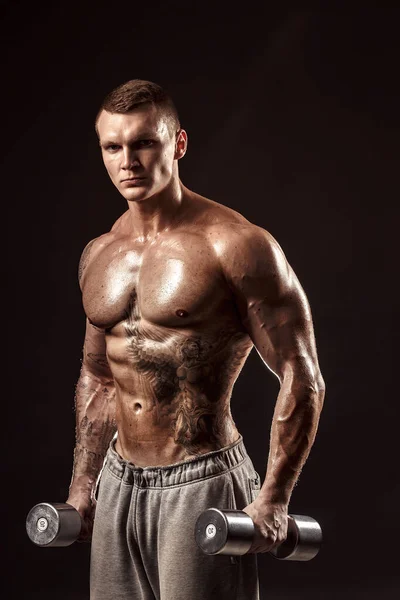Ernstige getatoeëerde shirtloze atleet tillen metalen halters training op donkere achtergrond — Stockfoto
