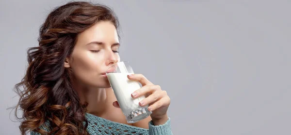 Feliz jovem mulher bebendo leite sobre fundo cinza — Fotografia de Stock
