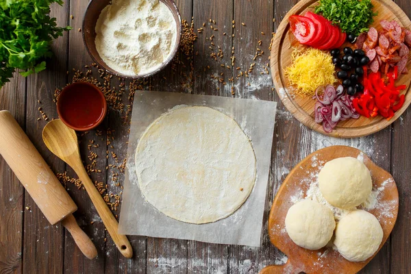 Tahta masadaki malzemeli pizza hamuru.
