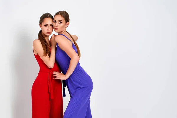 Twee meisjes staan in studio in elegante kleurrijke overalls op witte achtergrond — Stockfoto