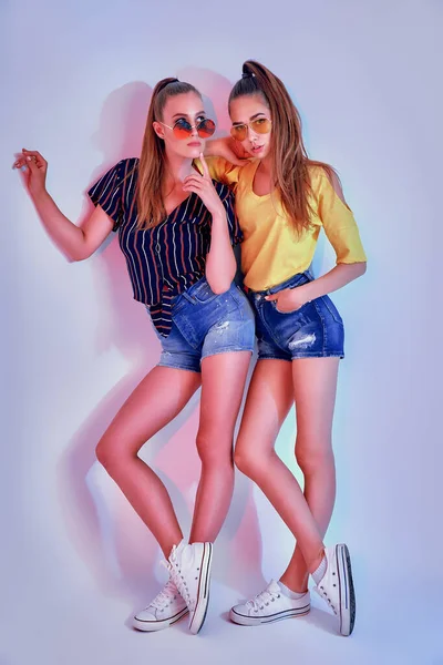 Δύο γυναίκες έφηβοι με γυαλιά ηλίου και καλοκαιρινά ρούχα ποζάρουν στο στούντιο σε λευκό φόντο — Φωτογραφία Αρχείου