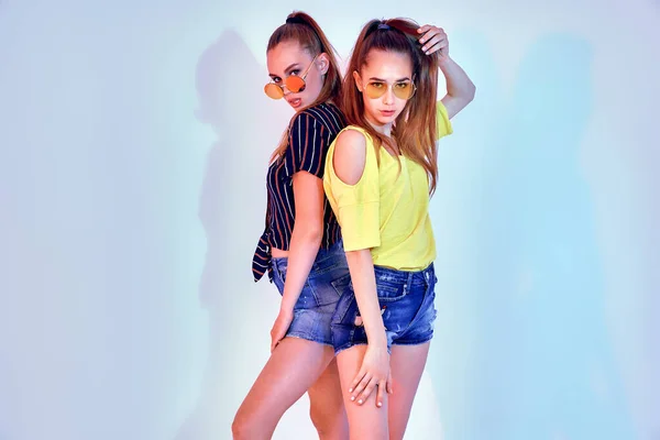 Две девушки-подростки в солнечных очках и летней одежде позируют в студии на белом фоне — стоковое фото