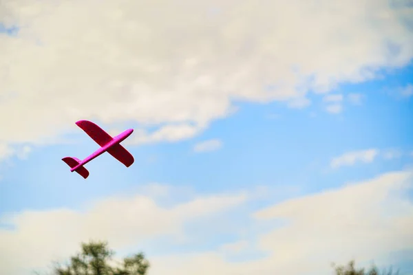 Ein rosafarbenes Kinderflugzeug aus Plastik fliegt in blauem Himmel umgeben von weißen Wolken — Stockfoto