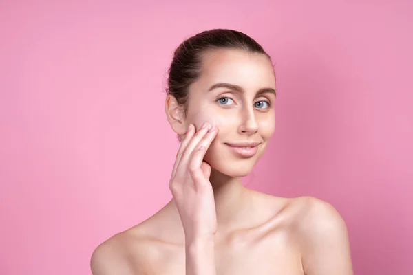 Mooie jonge vrouw aanbrengen crème op haar gezicht tegen kleur achtergrond — Stockfoto