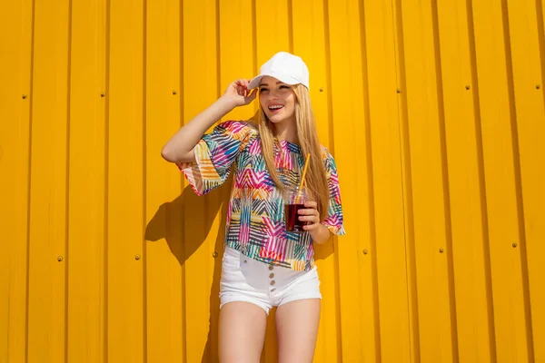 Menina estilo hipster muito jovem se divertir ao ar livre em boné branco e comer sorvete no fundo amarelo estilo urbano — Fotografia de Stock