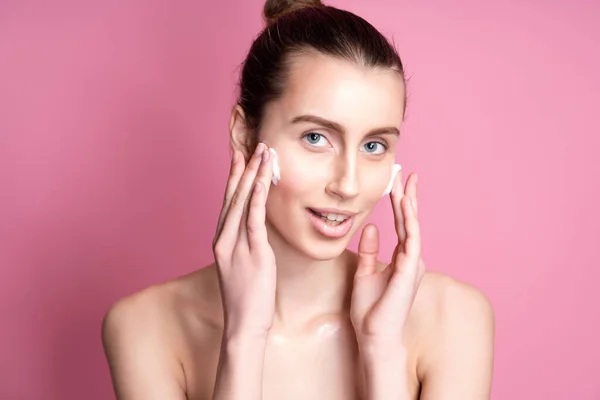 Gyönyörű fiatal nő alkalmazása krém az arcára ellen színes háttér — Stock Fotó