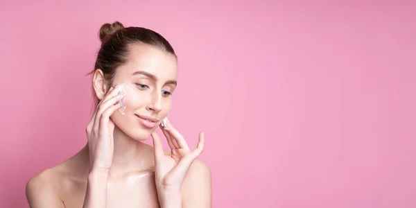 Bella giovane donna applicando crema sul suo viso contro lo sfondo di colore — Foto Stock