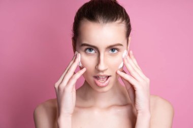 Güzel genç bir kadın yüzüne krem sürüyor.