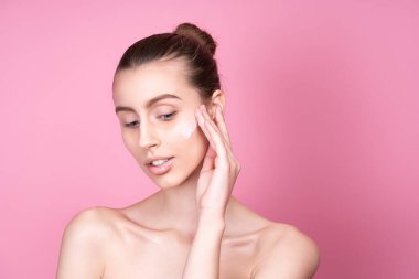 Güzel genç bir kadın yüzüne krem sürüyor.