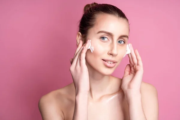 Mooie jonge vrouw aanbrengen crème op haar gezicht tegen kleur achtergrond — Stockfoto