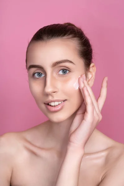 Mooie jonge vrouw aanbrengen crème op haar gezicht tegen kleur achtergrond — Stockfoto