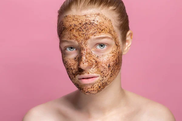 Mascarilla facial exfoliante Café molido máscara en la cara de una hermosa mujer joven Cosmetología orgánica natural Rosado fondo del estudio Aislar —  Fotos de Stock