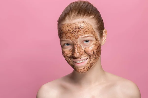 Facial skin scrub Coffee grounds mask on the face of a beautiful young woman Organic natural cosmetology Pink studio background Isolate — Stock Photo, Image