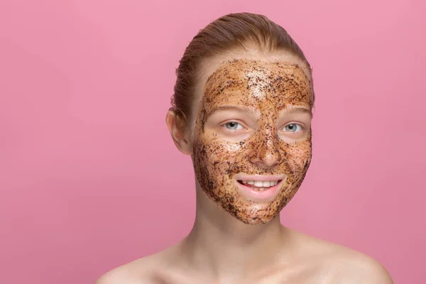 Facial skin scrub Coffee grounds mask on the face of a beautiful young woman Organic natural cosmetology Pink studio background Isolate