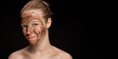 Genç ve güzel bir kadının yüzünde cilt kremi maskesi. Organik doğal kozmetoloji. Karanlık stüdyo arka planı.