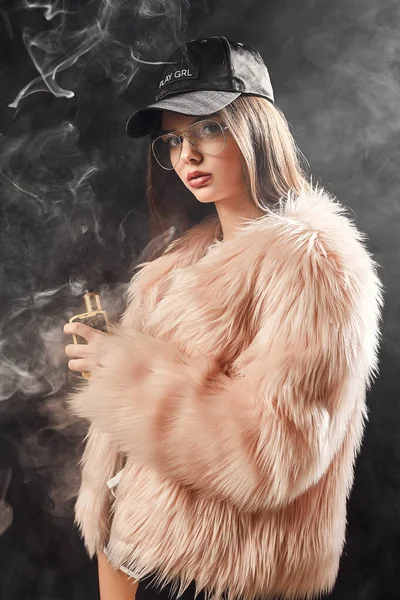 Femeia sexy la modă rap în haină de blană roz și țigară electronică de fum de capac. Dark Studio filmare fundal — Fotografie, imagine de stoc