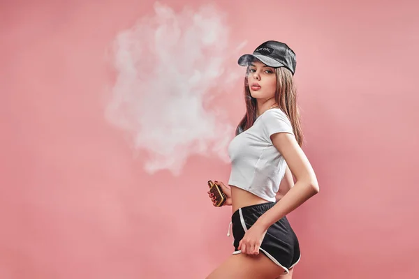 Seductive glamour young woman standing and vaping on pink background — Stock Photo, Image