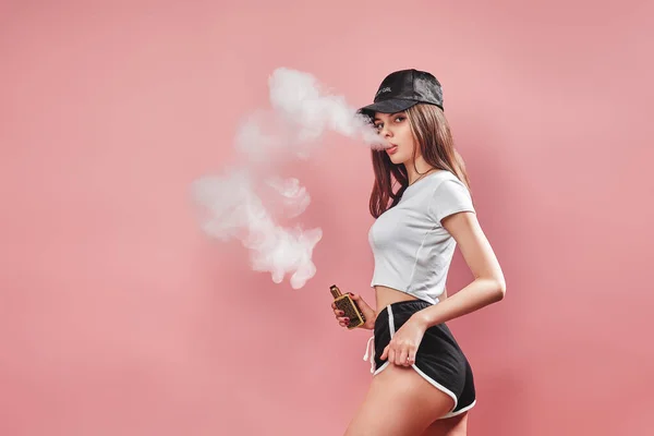 Seductive glamour young woman standing and vaping on pink background — Stock Photo, Image