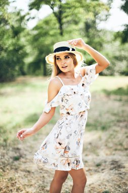 Yazlık elbisesi ve açık havada poz veren hasır şapkalı güzel ve narin bir kadın. Müthiş sıcak yaz günü