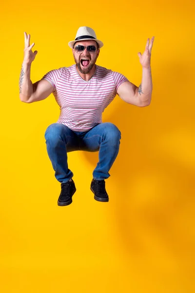 Opgewonden jonge bebaarde fitness sportieve man met hoed en zonnebril Springen zeer emotioneel geïsoleerd op gele achtergrond — Stockfoto