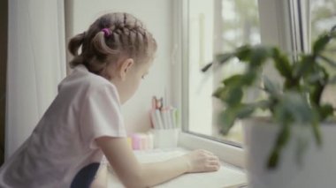 Güzel küçük kız pencerenin yanında oturmuş kitap okuyor, dışarıda yağmur yağıyor.