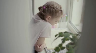 Güzel küçük kız pencerenin yanında oturmuş kitap okuyor, dışarıda yağmur yağıyor.