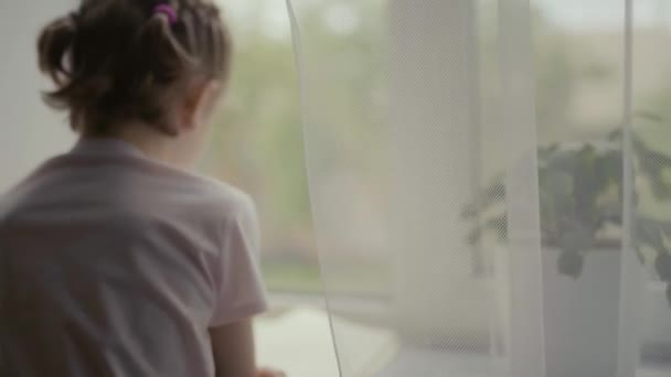 Krásná holčička čte knihu, která sedí u okna, venku prší — Stock video