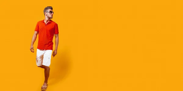 Full length portret van een knappe man in korte broek en rood shirt lopen en kijken zijwaarts geïsoleerd op gele achtergrond. Summertime-concept — Stockfoto