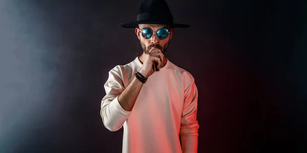 Stylish man in sunglasses puffing the vapor on the black background — Stock Photo, Image