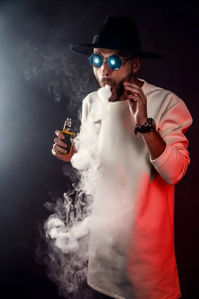 Stylish man in sunglasses puffing the vapor on the black background — Stock Photo, Image