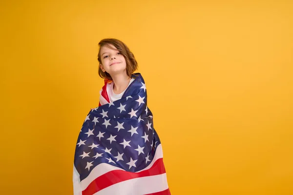 Šťastné dítě, roztomilá dívka s americkou vlajkou na žlutém pozadí studia. USA slaví 4. července, Den nezávislosti. — Stock fotografie