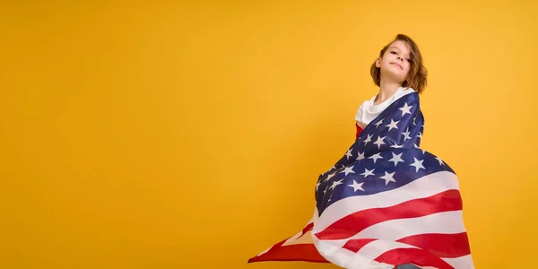Šťastné dítě, roztomilá dívka s americkou vlajkou na žlutém pozadí studia. USA slaví 4. července, Den nezávislosti. — Stock fotografie