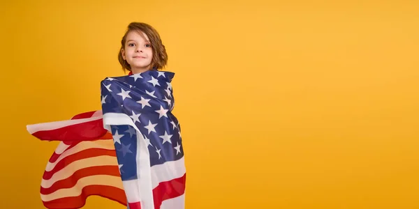 Šťastné dítě, roztomilá dívka s americkou vlajkou na žlutém pozadí studia. USA slaví 4. července, Den nezávislosti. — Stock fotografie